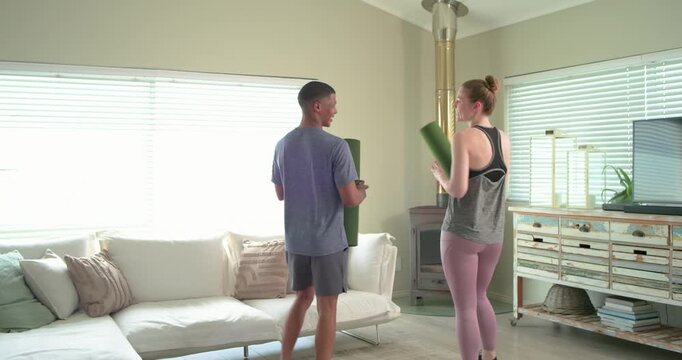Diverse friends in gym wear entering home carrying green mats, unrolling and kneeling starting yoga