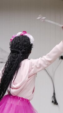 Vertical video: Grinning girl dancing on porch in tutu, waving wand, holding bucket for Halloween