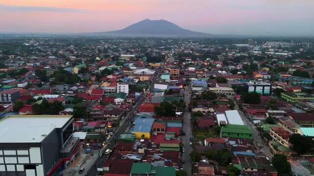 A cinematic wide aerial shot capturing the dense urban sprawl of Angeles City in the Philippines, with the majestic Mount Arayat volcano silhouetted against a soft sunset sky
