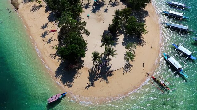 High-angle drone shot of Cowrie Island, Palawan. Features traditional outrigger boats docked on the sandy beach surrounded by turquoise tropical waters. Scenic island nature landscape
