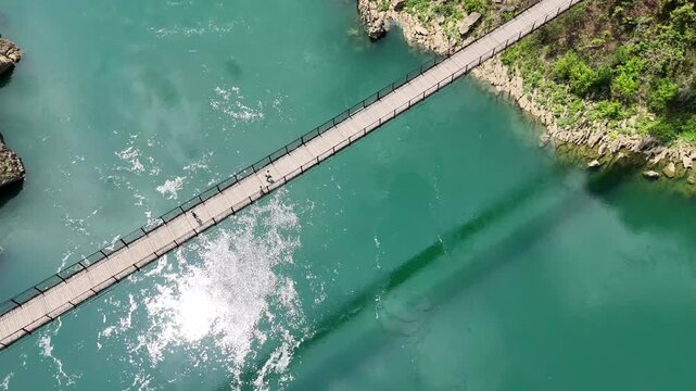 Daily Passage: Several People Crossing the Historic Iron Bridge Over Turquoise Waters