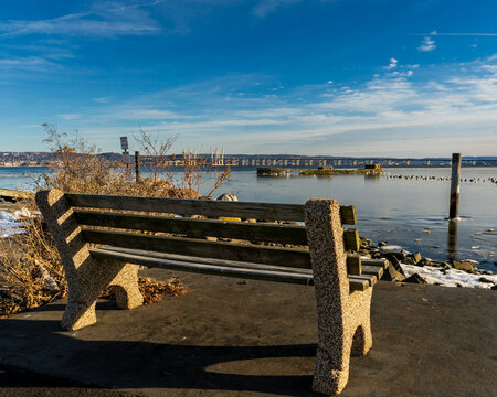 Nyack, NY - US - Jan 24, 2026 Serene winter waterfront in Nyack, NY, with a concrete bench overlooking a partly frozen Hudson River and the Mario M. Cuomo Bridge beneath a bright blue sky.