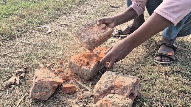 Professional cinematic video of a young man breaking bricks to make chips under the scorching sun, Labor & Construction in Bangladesh, 4K UHD 30fps.