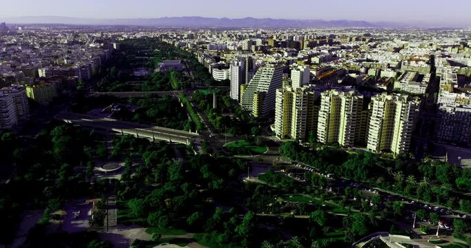Drone aerial wide over Valencia Spain cityscape, modern apartment towers rising above Turia Gardens park corridor, cinematic skyline establishing shot at golden hour