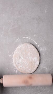 Overhead view of raw chinese scallion pancakes being rolled on grey countertop, top view of homemade scallion pancakes being shaped on countertop, process of making cong you bing