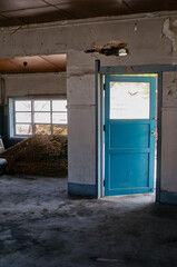Old rustic interior with a weathered blue wooden door and bundles of dried crops on the floor.