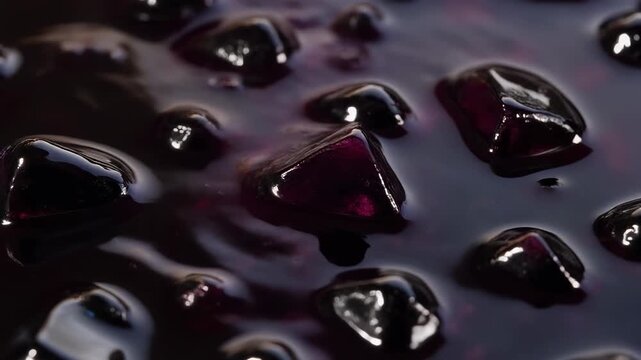 Macro shot of dark glossy fruit pieces submerged in thick purple syrup or jam creating a rich and luxurious texture background
