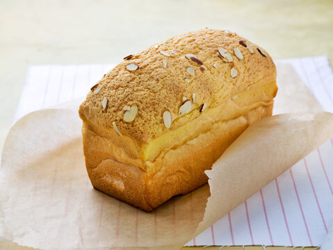 Freshly baked almond streusel bread loaf topped with sliced almonds on parchment paper.