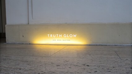 Soft Yellow Light Illuminates "Truth Glow" Sign on Plain Wall for Artistic Perspective and Reflective Ambiance