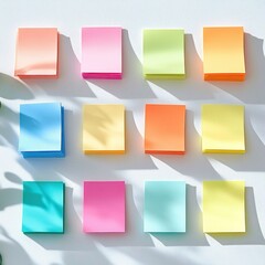 Fototapeta premium Neat grid of colorful pastel sticky note stacks on a white surface with soft leaf shadows and warm natural light, evoking calm cheerful organization and productivity