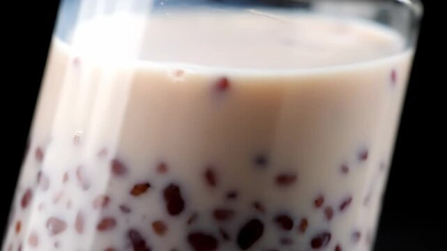 Macro close-up of sweet creamy beverage with red adzuki beans (possibly Boba or Red Bean Milk) served in a glass against a dark black background.