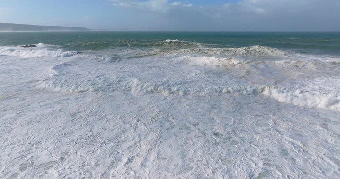 Drone aerial over Nazare Portugal Atlantic Ocean, foamy waves and heavy swell rolling toward shore, cinematic coastal seascape with dynamic surf lines