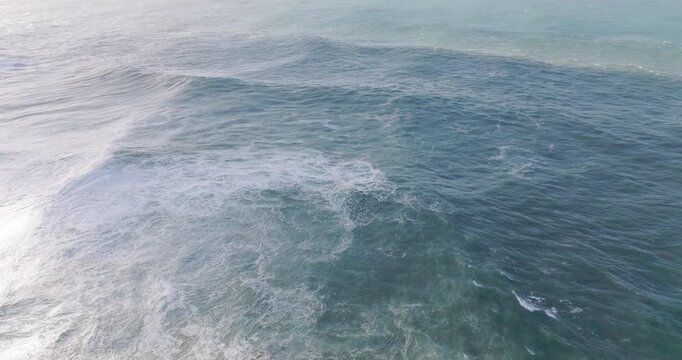 Drone aerial over open Atlantic off Nazare Portugal, wind-driven swell and textured ocean surface with whitecaps, cinematic seascape horizon and rolling waves