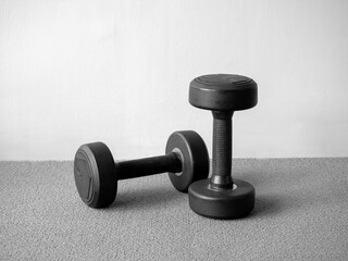 Black and white photo of two dumbbells on carpeted floor, symbolizing strength, discipline, and minimalist fitness lifestyle, perfect for gym concepts, workout motivation, and health promotion.