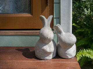 Two cement rabbit sculptures placed by a cozy window symbolize home decoration, Easter celebration, spring season, and cozy lifestyle. Perfect for festive and garden-themed interior concepts.