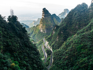 Scenic winding mountain road in Tianmen Mountain, Zhangjiajie, China, surrounded by lush green peaks and dramatic cliffs, ideal for adventure travel and nature exploration photography.