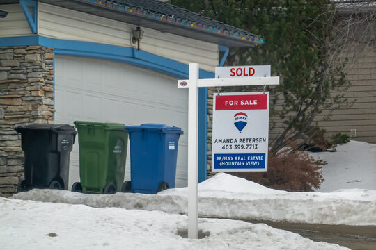 Calgary, Alberta, Canada. Jan 25, 2026. A REMAX real estate "Sold" sign standing in front of a suburban home next to residential recycling bins during winter.