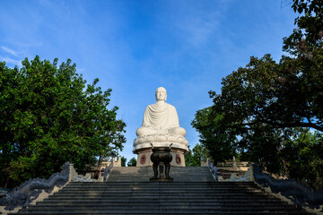 Obraz premium White Buddha statue at Long Son Pagoda in Nha Trang, Vietnam framed by trees and staircase
