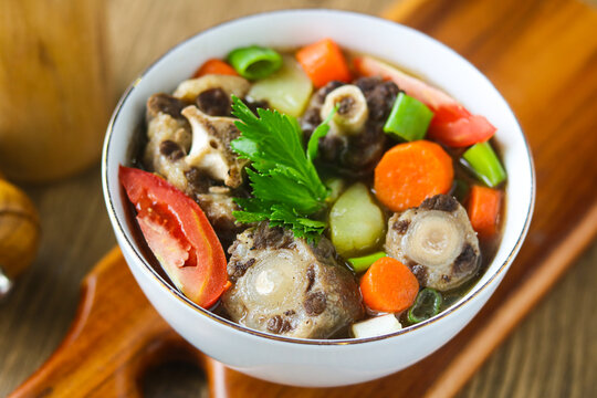 Closeup bowl of Oxtail Soup (Sop Buntut). This dish is served with nutrient-rich vegetables including chunks of carrot, potato, spring onion and fresh tomato wedges in a clear beef broth.