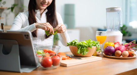 Close up of Asian woman chopping carrot on cutting board with fresh vegetables and fruits. Healthy...