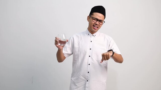 Muslim men waiting for the time to break the fast, looking at the clock while carrying water in a glass, drinking water at the time to break the fast.