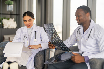 Obraz premium African american male doctor analyzing brain MRI X-ray with female colleague in hospital, medical team consultation, diversity healthcare specialists discussing radiology diagnosis results together