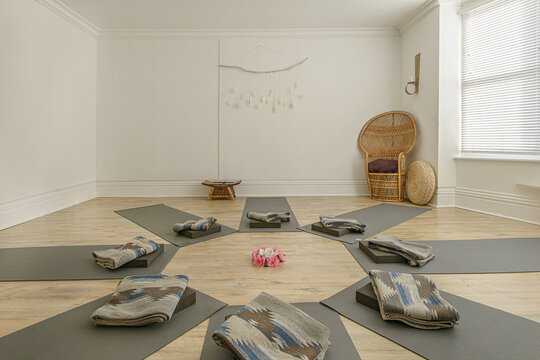 Sunlight yoga studio featuring mats arranged in a circle with blankets, cushions, and a wicker chair for group meditation.