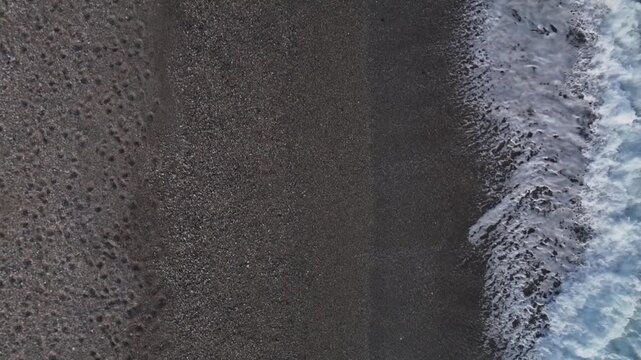 Aerial view of waves crashing onto a pebbly beach, serene and calm