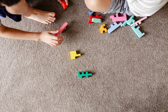 Two children seated on carpeted floor playing with blocks