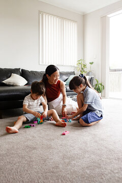 Two children seated on carpeted floor playing with blocks with mum nearby in living room