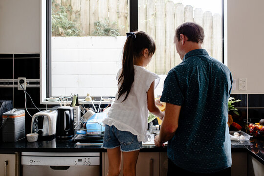 Father teaching daughter how to wash dishes in the kitchen