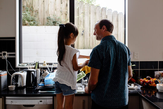 Father teaching daughter how to wash dishes in the kitchen