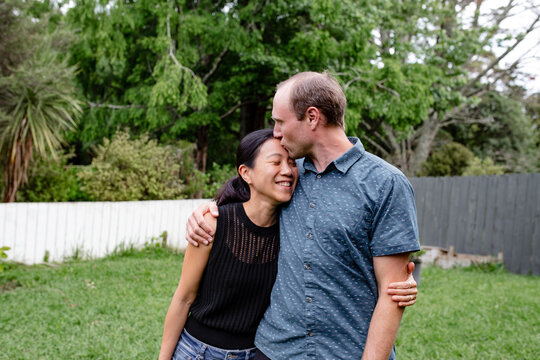 Couple with mixed ethnicity standing in the backyard giving wife a kiss on forehead