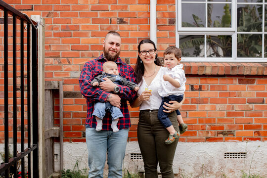 Happy couple standing in front of a brick wall holding an infant and toddler son