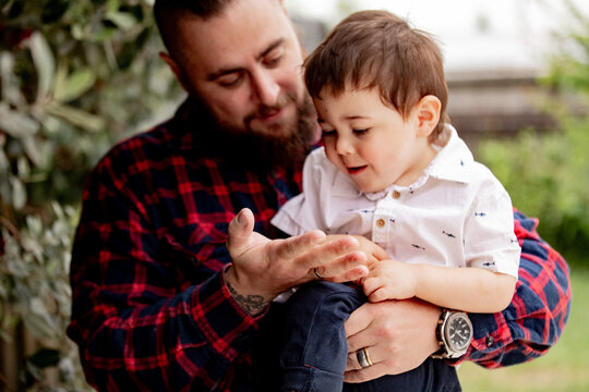 Father in red checkered shirt carrying toddler son showing bug on his palm