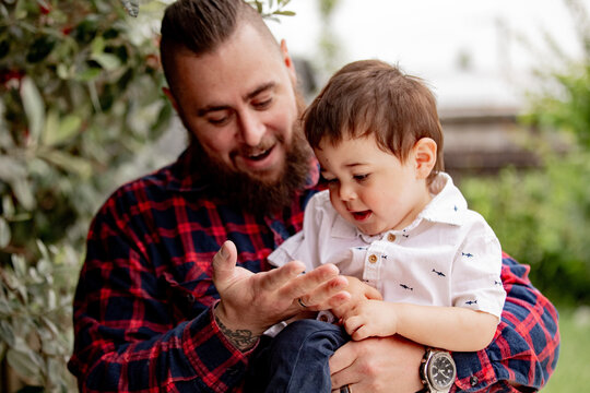 Father in red checkered shirt carrying toddler son showing bug on his palm
