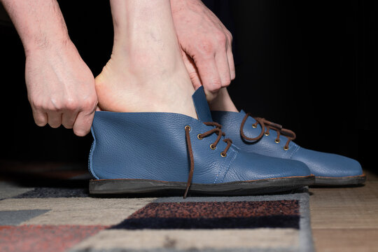 Close-up of a person putting on a stylish blue leather shoe with brown laces, highlighting the process of dressing. Focus on footwear, hands, and a casual indoor setting.