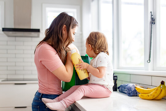 Toddler girl seated on kitchen counter helping mum unpack shopping bag