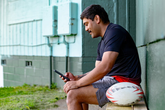 Samoan rugby player sitting on wooden bench holding a phone