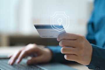 Close-up of hands holding a credit card during online payment with security shield icon overlay. Concept of secure transaction, identity protection, fraud prevention, and financial authentication.