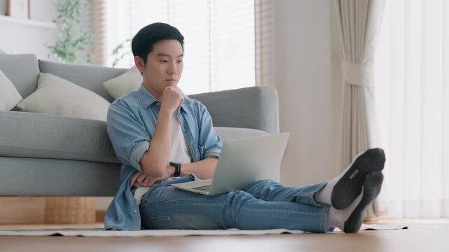 Young Asian man relaxing on comfortable couch, using laptop at home, happy boy chatting with friends in social network, spending weekend, watching movie, shopping online