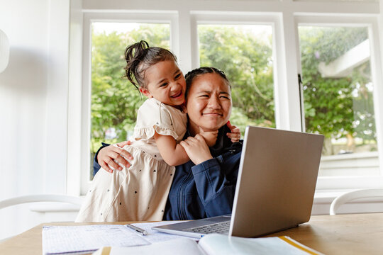 Toddler girl hugging teen sister while doing her homework