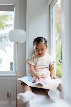 Young samoan girl reading a book while sitting by the windowsill