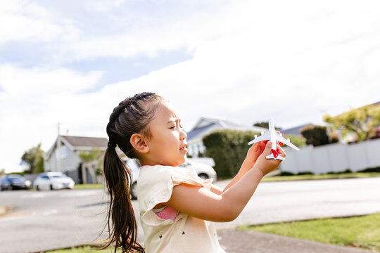 Young Samoan girl holding a toy aeroplane up in the air outdoors - travel concept