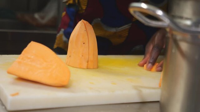 Close-up shows a woman chef cutting yam into concass&eacute; cubes on a kitchen board while preparing a traditional recipe in slow motion.