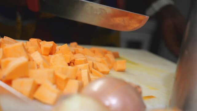 Slow motion kitchen scene shows a woman chef preparing yam (Dioscorea spp.) and sweet potato (Ipomoea batatas), known as igname, &ntilde;ame, inhame, batata, sliced into concass&eacute; for traditional veloute soup