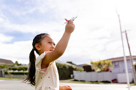 Young Samoan girl holding a toy aeroplane up in the air outdoors - travel concept