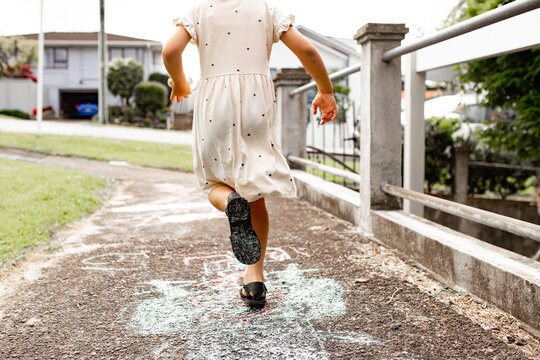 Girl skipping down urban pathway covered in chalk drawings