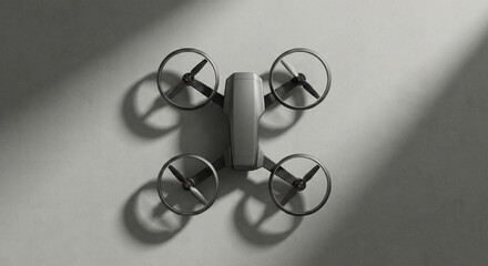 A high-angle, minimalist shot of a professional quadcopter drone with propeller guards and carbon fiber arms, featuring dramatic shadows on a textured grey surface. (187 characters)