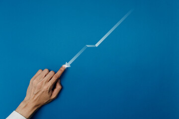 Businessman hand pointing at a falling zig-zag arrow on a blue background. Concept for financial loss, economic crisis, market downturn, business failure, risk management, and solving problems.